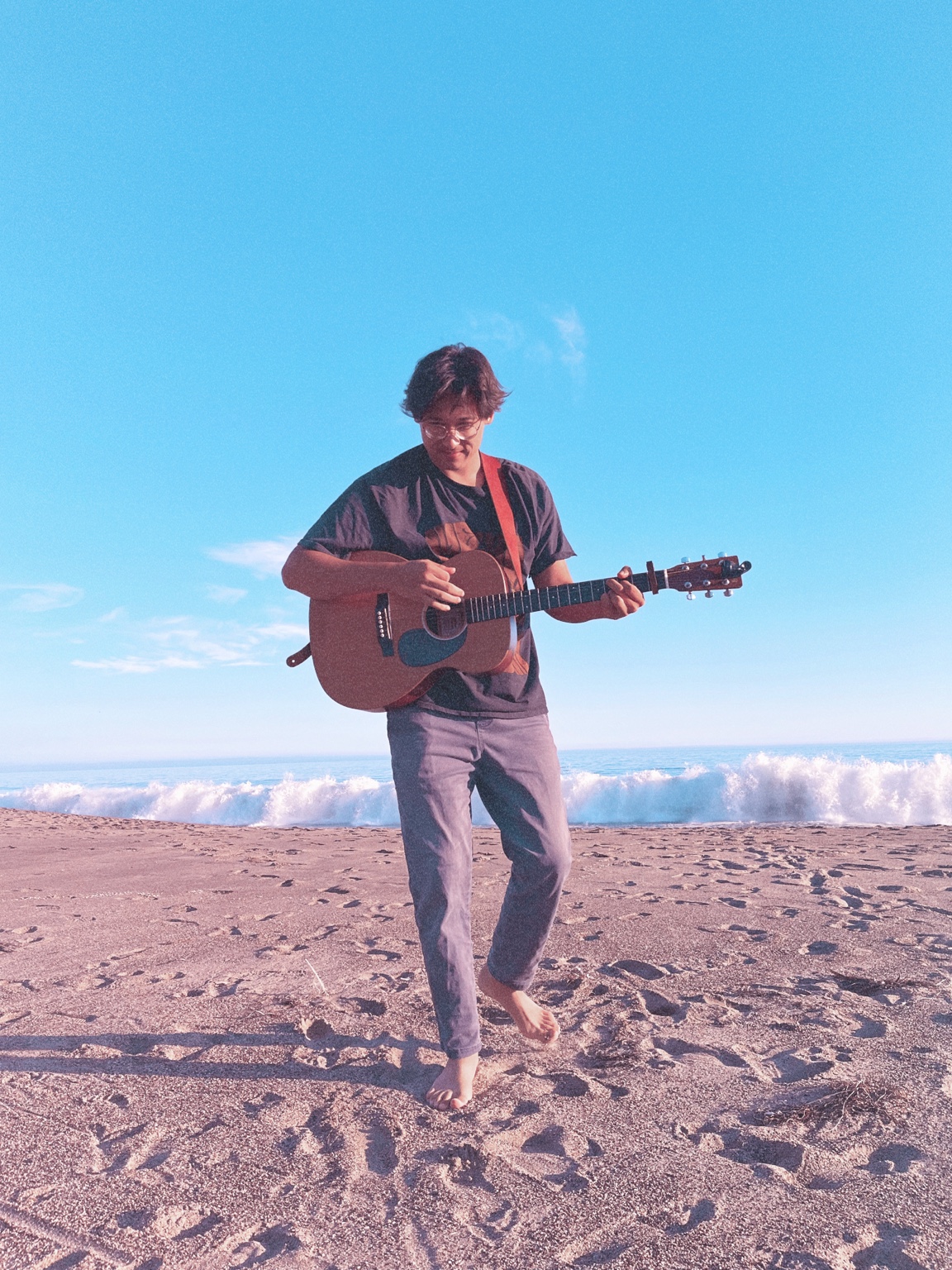 Noah holding an acoustic guitar on the beach